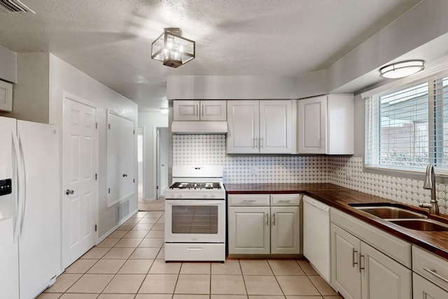 kitchen featuring dark countertops, visible vents, under cabinet range hood, white appliances, and a sink