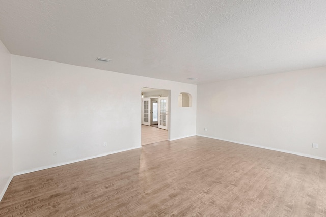 empty room featuring visible vents, light wood-style flooring, a textured ceiling, arched walkways, and baseboards