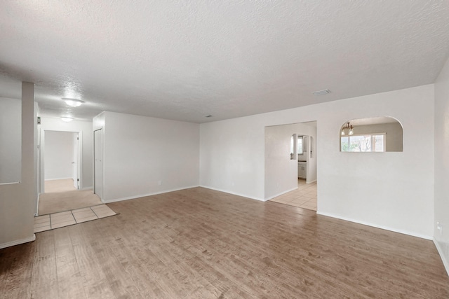 empty room with baseboards, light wood-style floors, arched walkways, and a textured ceiling