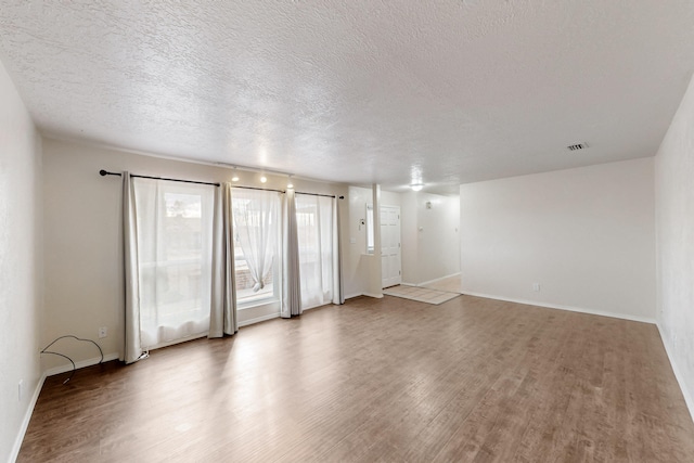 unfurnished living room with visible vents, a textured ceiling, baseboards, and wood finished floors