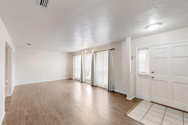 foyer entrance featuring visible vents, light wood-type flooring, and a textured ceiling