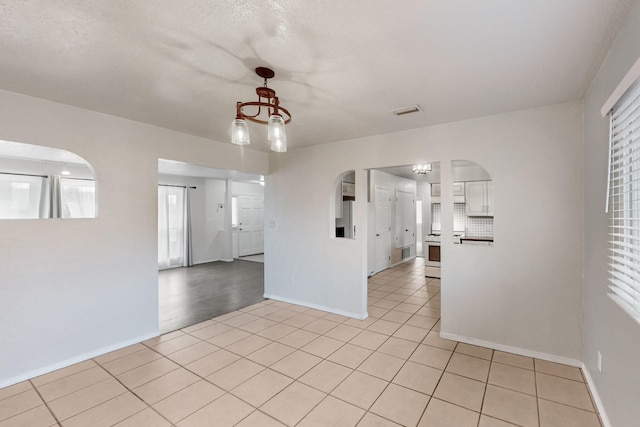 empty room featuring light tile patterned floors, visible vents, and arched walkways