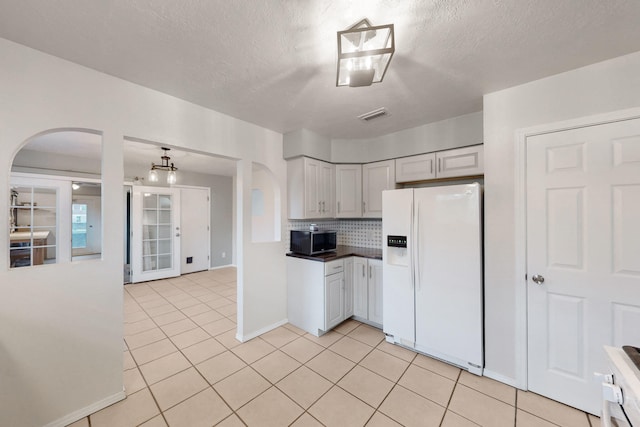 kitchen featuring visible vents, stainless steel microwave, arched walkways, white fridge with ice dispenser, and light tile patterned floors