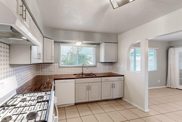 kitchen featuring white appliances, light tile patterned floors, a sink, under cabinet range hood, and backsplash