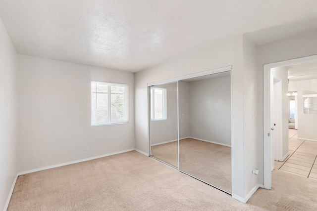 unfurnished bedroom with light carpet, a textured ceiling, baseboards, and a closet