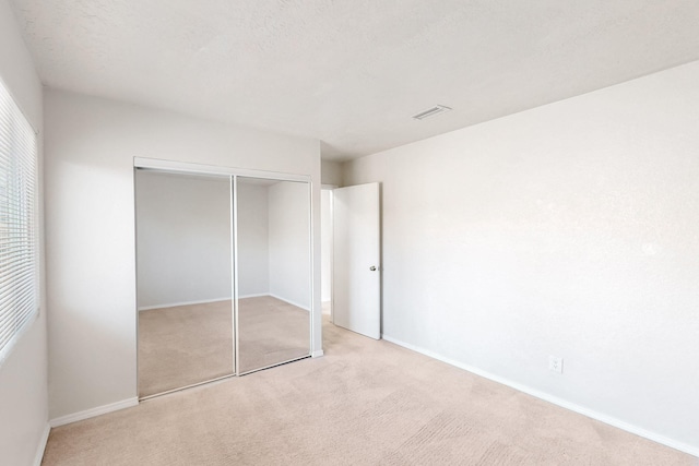 unfurnished bedroom featuring visible vents, baseboards, light colored carpet, a closet, and a textured ceiling