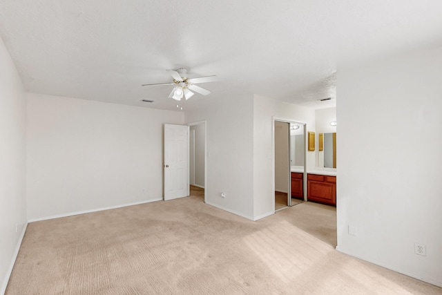 unfurnished bedroom with baseboards, light colored carpet, ensuite bath, and a ceiling fan