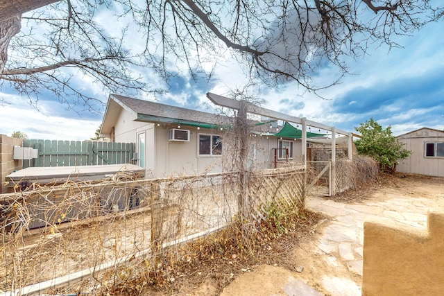 rear view of property with an AC wall unit, an outdoor structure, a shed, and fence