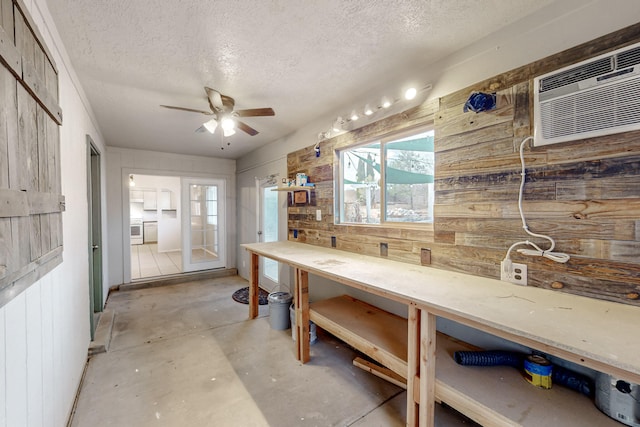 kitchen with a wall mounted air conditioner, a ceiling fan, a textured ceiling, concrete floors, and wood walls