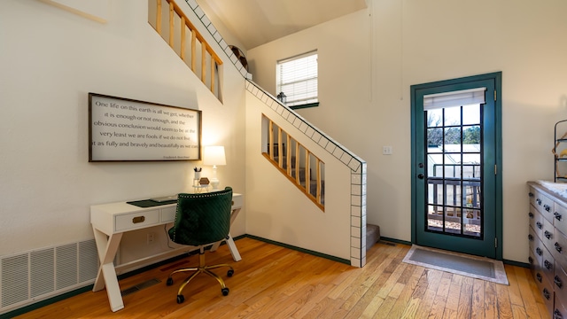 home office featuring light wood-style flooring, visible vents, a high ceiling, and baseboards