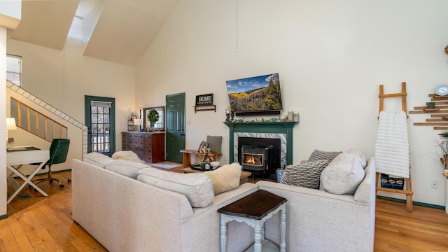 living area with light wood finished floors, high vaulted ceiling, stairs, and a wood stove