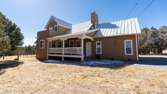 exterior space featuring a standing seam roof, a porch, stucco siding, a chimney, and metal roof