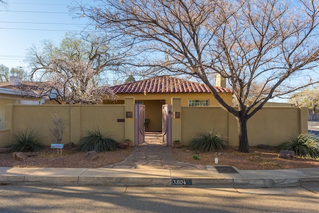 mediterranean / spanish-style house with a gate, a chimney, stucco siding, a fenced front yard, and a tile roof