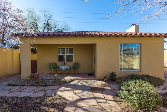 back of house with stucco siding, a tiled roof, and a chimney