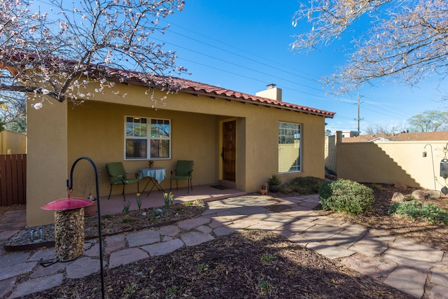 back of house with stucco siding, a tile roof, fence, covered porch, and a chimney