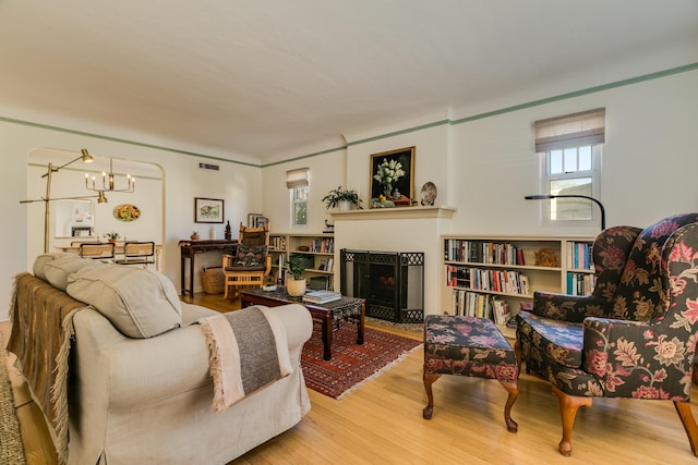 living area with a chandelier, a fireplace with flush hearth, visible vents, and wood finished floors