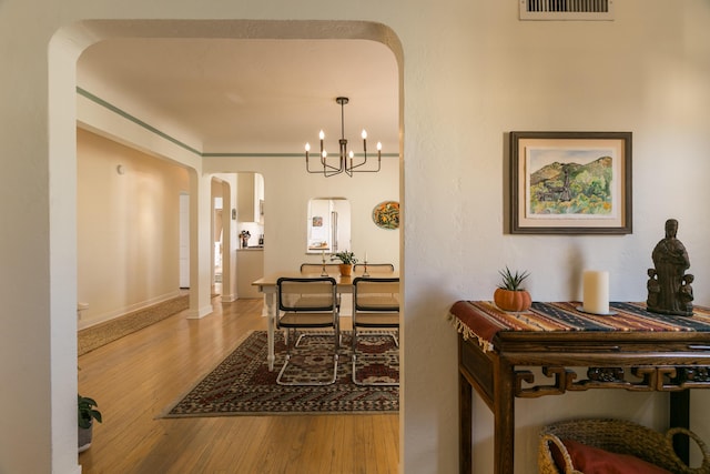 dining space with visible vents, baseboards, a chandelier, wood finished floors, and arched walkways