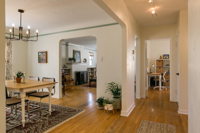 hall featuring a notable chandelier, wood finished floors, arched walkways, and baseboards