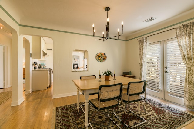 dining space with visible vents, baseboards, light wood-style flooring, an inviting chandelier, and arched walkways