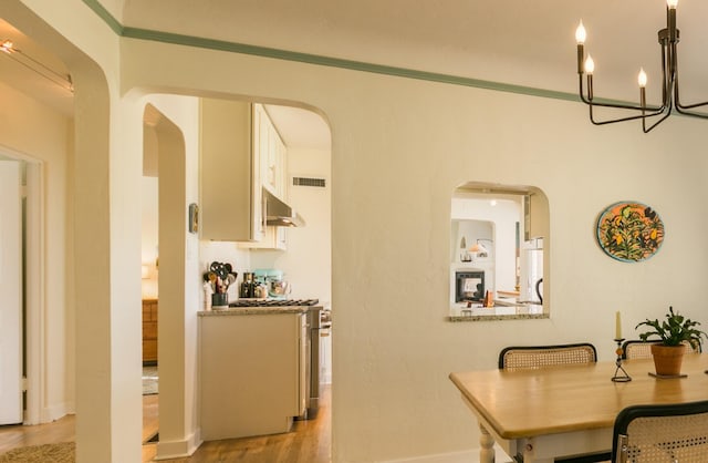 dining space with visible vents, crown molding, light wood-style flooring, arched walkways, and a notable chandelier