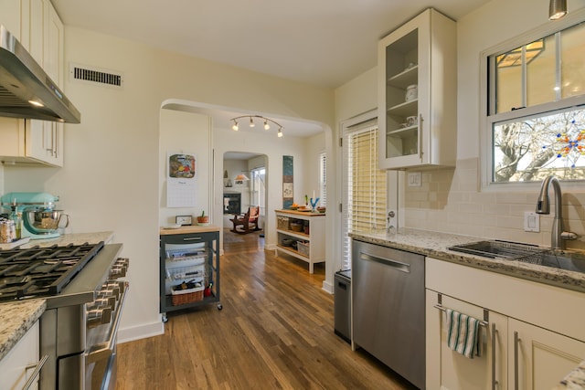 kitchen with visible vents, a sink, stainless steel appliances, arched walkways, and wall chimney range hood