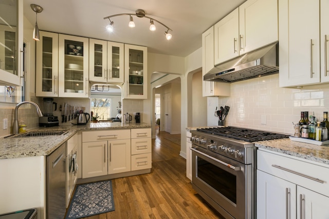 kitchen featuring light stone countertops, wood finished floors, a sink, high end stove, and under cabinet range hood