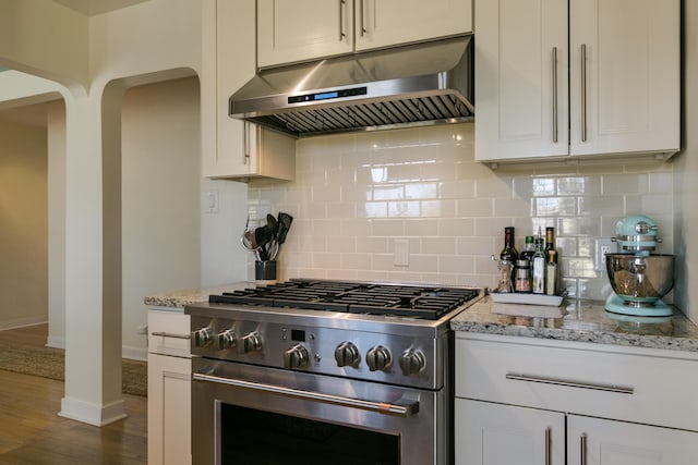 kitchen with light stone countertops, arched walkways, under cabinet range hood, and high end stainless steel range