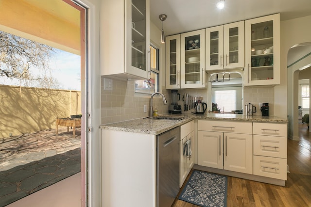 kitchen featuring dark wood finished floors, dishwasher, light stone counters, arched walkways, and a sink