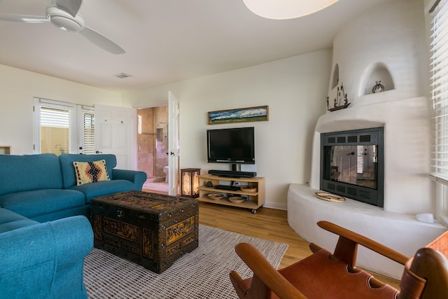 living area featuring wood finished floors, baseboards, visible vents, a ceiling fan, and a glass covered fireplace