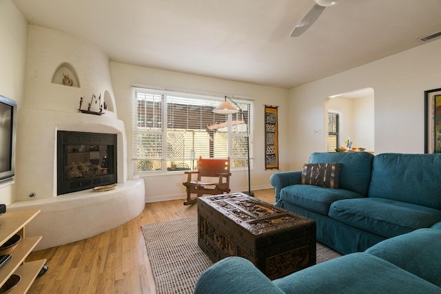 living room with visible vents, ceiling fan, a fireplace, wood finished floors, and arched walkways