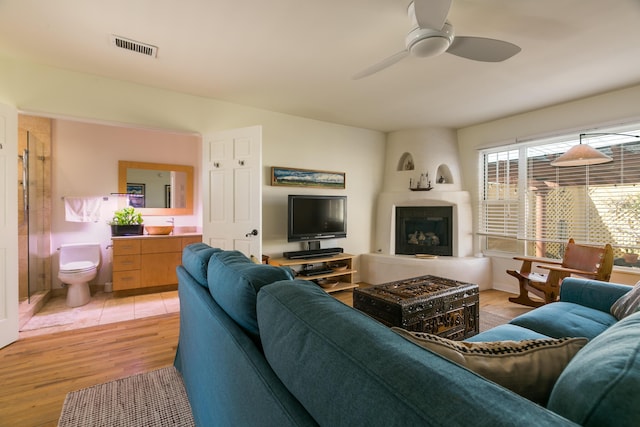 living area featuring visible vents, ceiling fan, a large fireplace, and light wood-style floors