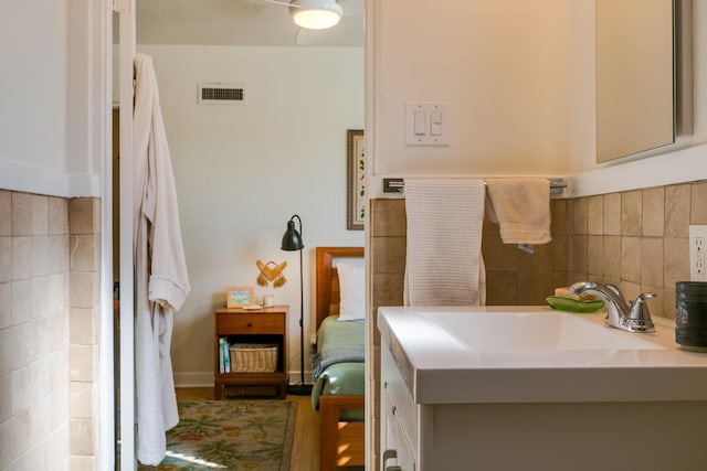 bathroom with vanity, decorative backsplash, tile walls, and visible vents