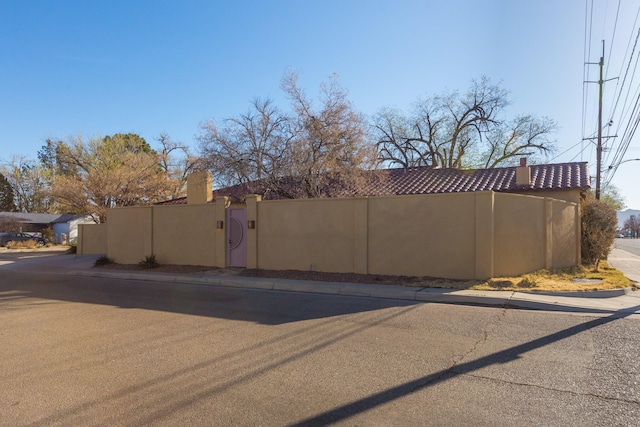 exterior space featuring stucco siding, a tiled roof, fence, and a chimney