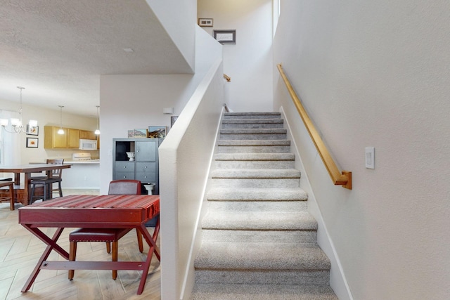 stairway with baseboards, a notable chandelier, and a textured ceiling