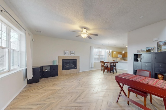 living area featuring visible vents, a ceiling fan, a textured ceiling, baseboards, and a tile fireplace