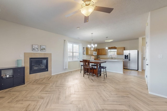 dining room featuring baseboards, a textured ceiling, ceiling fan with notable chandelier, and a tile fireplace