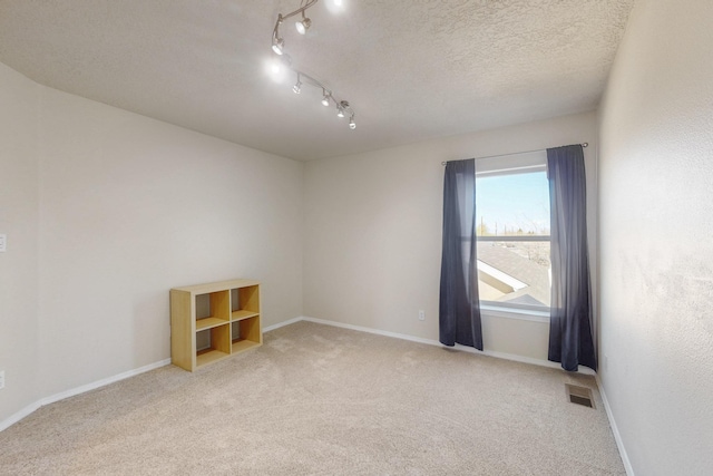 spare room featuring light carpet, visible vents, a textured ceiling, and baseboards