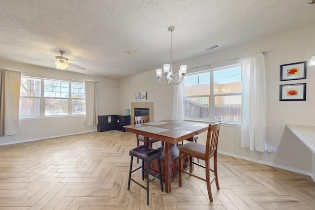 dining room featuring visible vents, a tiled fireplace, ceiling fan with notable chandelier, a textured ceiling, and baseboards