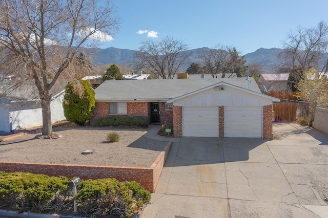 ranch-style home featuring driveway, fence, a mountain view, an attached garage, and brick siding