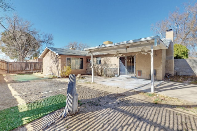 rear view of property featuring fence, ceiling fan, a chimney, stucco siding, and a patio area