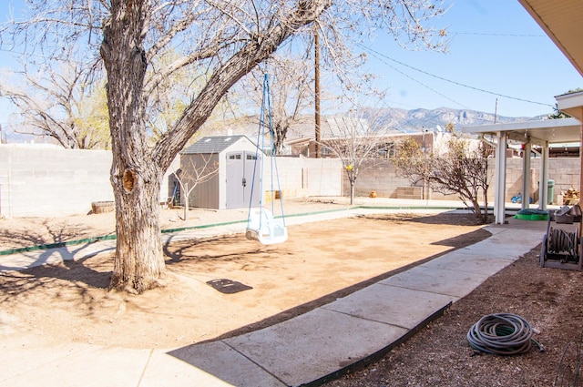 view of yard featuring a storage shed, an outbuilding, a fenced backyard, and a mountain view