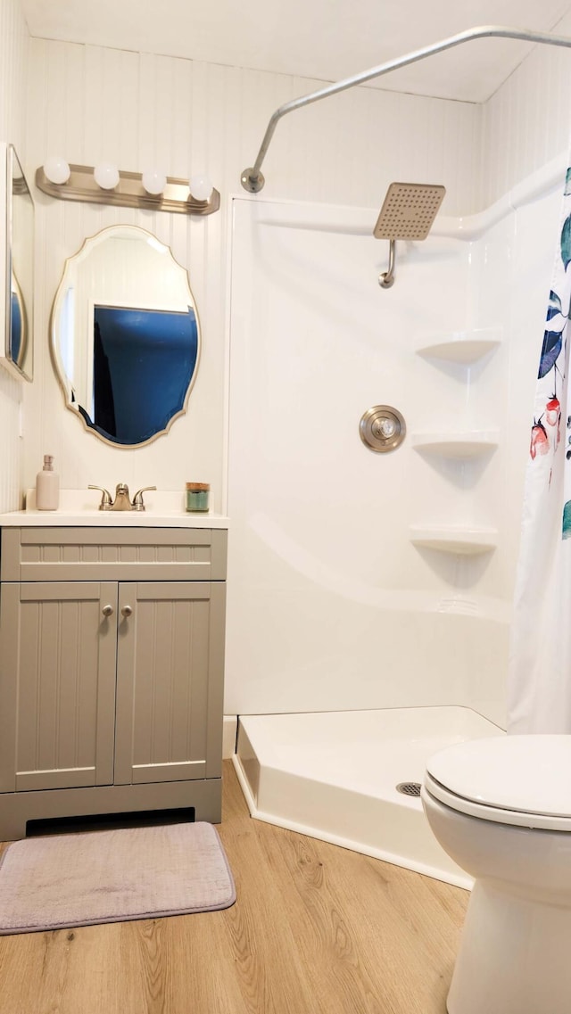 bathroom featuring vanity, toilet, wood finished floors, and a stall shower