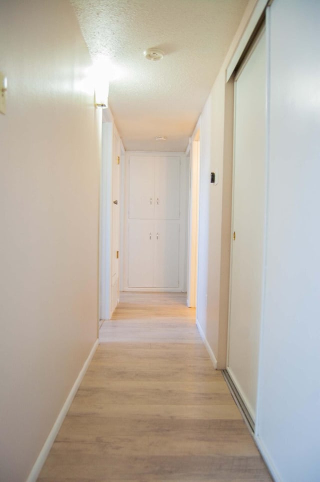 corridor with baseboards, a textured ceiling, and light wood-style flooring