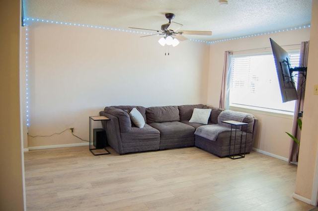 living area with light wood-style flooring, a ceiling fan, baseboards, and a textured ceiling