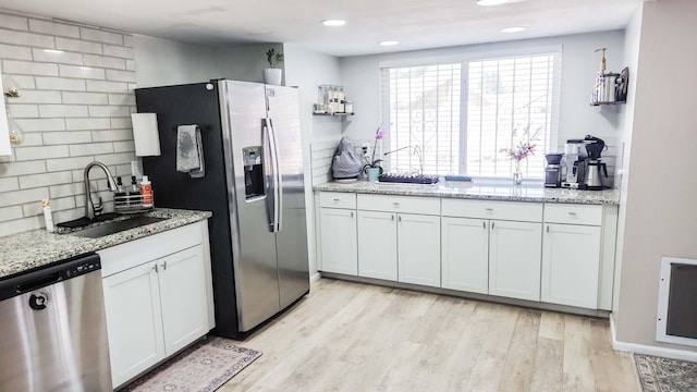 kitchen with light stone counters, decorative backsplash, light wood-style flooring, stainless steel appliances, and a sink