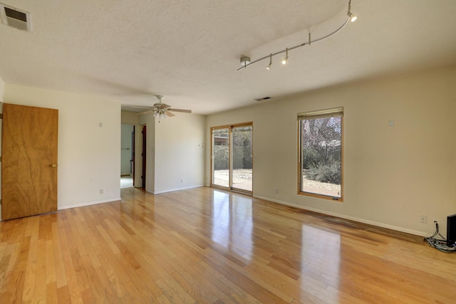 empty room featuring baseboards, visible vents, ceiling fan, light wood-style floors, and a textured ceiling