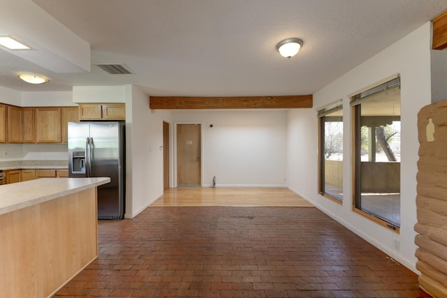 kitchen featuring visible vents, stainless steel fridge with ice dispenser, light countertops, brick floor, and baseboards