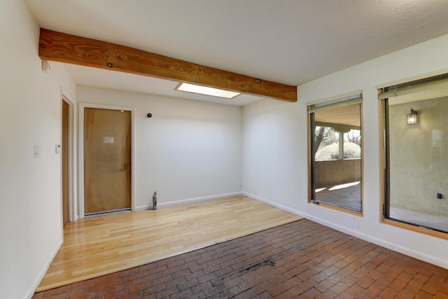 unfurnished room featuring brick floor, baseboards, beam ceiling, and a skylight