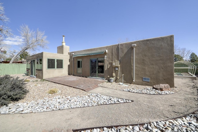 back of property with fence, a patio area, a chimney, and stucco siding