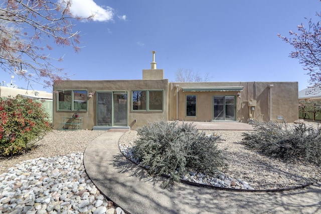 rear view of house with stucco siding and a chimney